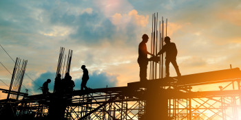 Image of workers building a structure with a setting sun behind them