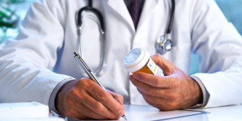 A picture of a doctor holding a bottle of prescription pills while writing on a notepad